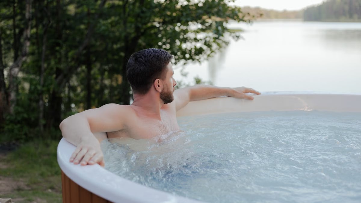 A man enjoys a serene moment in a jacuzzi overlooking a peaceful lake.